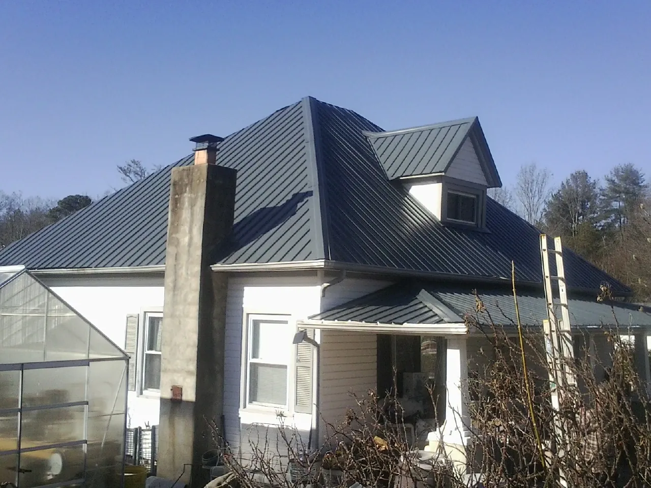 Dark blue standing seam metal roof on a white farmhouse with dormer — Slate & Tile Roof Repair by Roofing Brothers in Jetersville