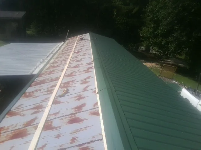 Old rusted panels beside newly installed green metal roofing — Wind Damage Roof Repair by Roofing Brothers in Jetersville