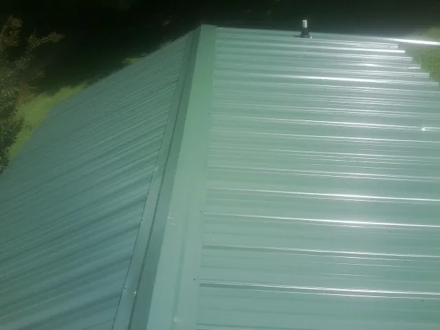 New green metal panels meeting at the ridge of a roof — Flat Roof Repair work by our crew in Jetersville