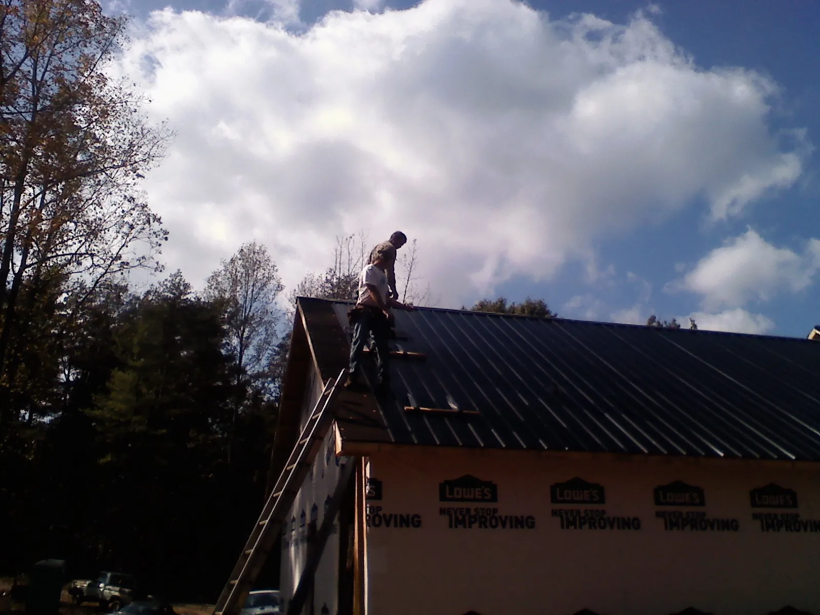 Roofer fastening dark metal panels high against a cloudy sky, from a Roof Inspection job in Jetersville