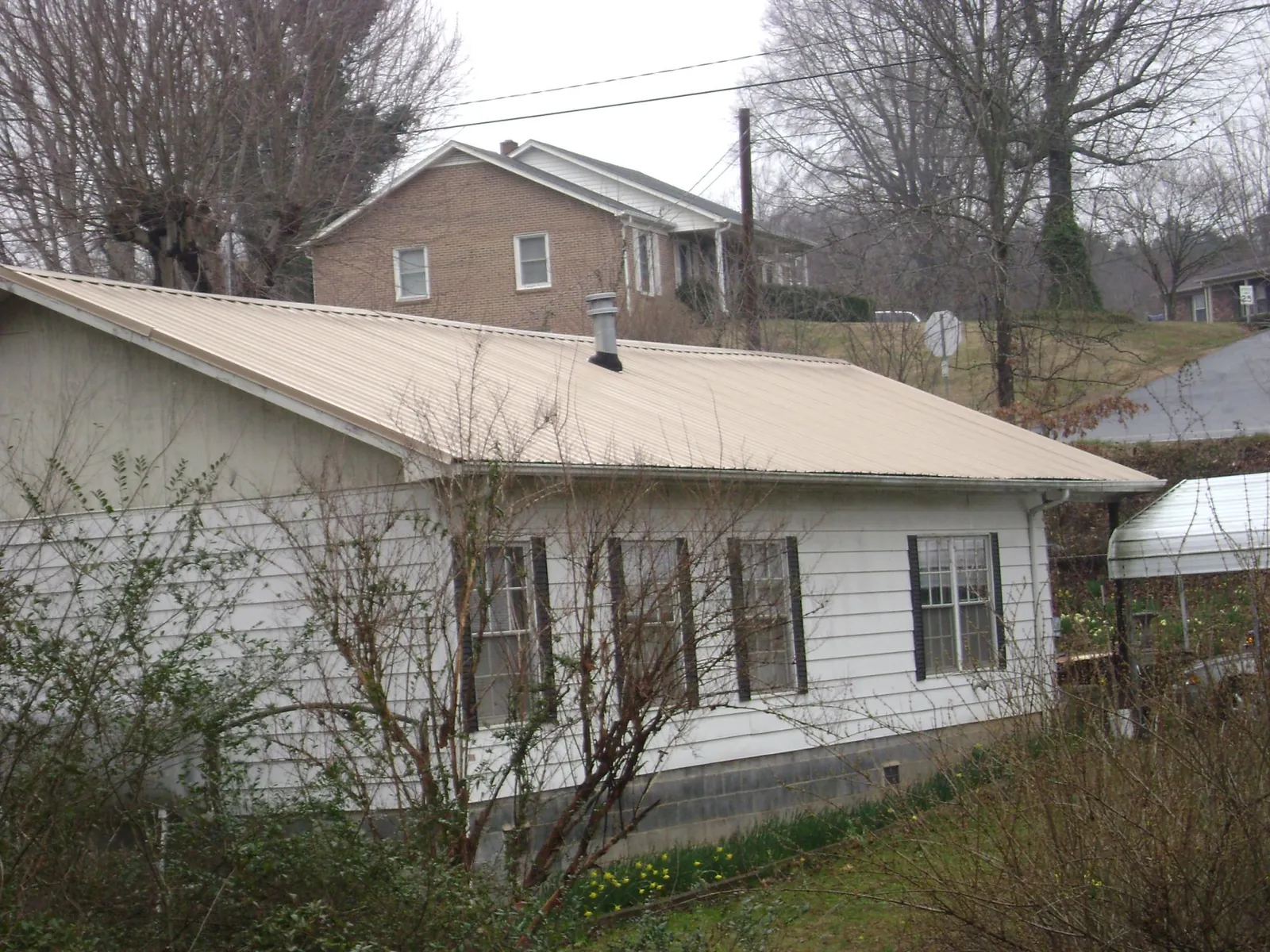 Tan metal roof on a white sided house set into a hillside — Commercial Roofing by Roofing Brothers in Jetersville